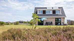 A modern two-story house with a flat roof, large windows, and a patio area with outdoor furniture. - Stylish Texel Escape With Spa (Den Burg)