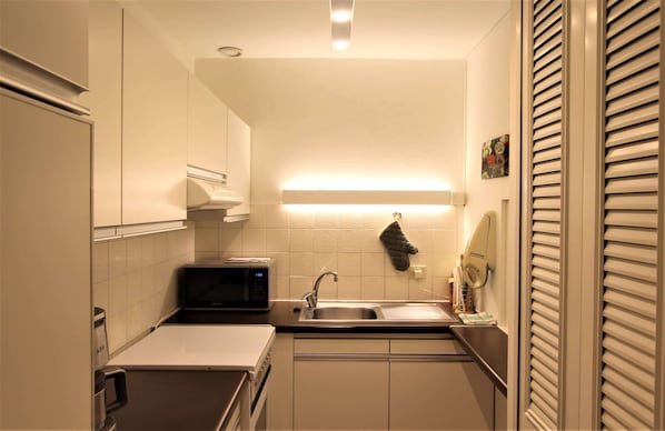 Cocina pequeña equipada con microondas, lavamanos y armarios.