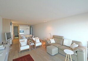 A modern living room with a sofa, armchairs, a TV, and a dining area. - Apartment in Het Zoute With Sea Views (Knokke-Heist)