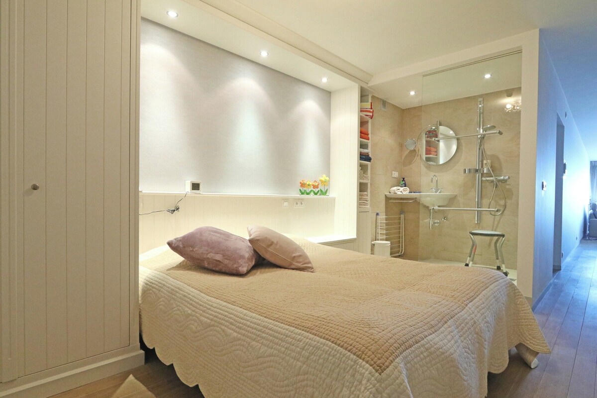 Un dormitorio con cama, mesita de noche, espejo y zona de ducha.