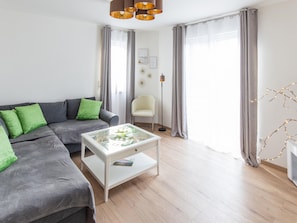 Ein modernes Wohnzimmer mit einem grauen Sofa, einem Glastisch, einer Stehlampe und einem Sessel.