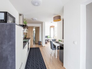 A modern kitchen with a microwave, a dining area with a table and chairs, and a hallway leading to another room. - Gemutliche Ferienwohnung, Beilngries (Beilngries)