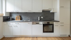A modern kitchen with white cabinets, a black countertop, a coffee maker, a kettle, and an oven. - Chalet in Turracher Hohe With Ski Slope Access (Reichenau)