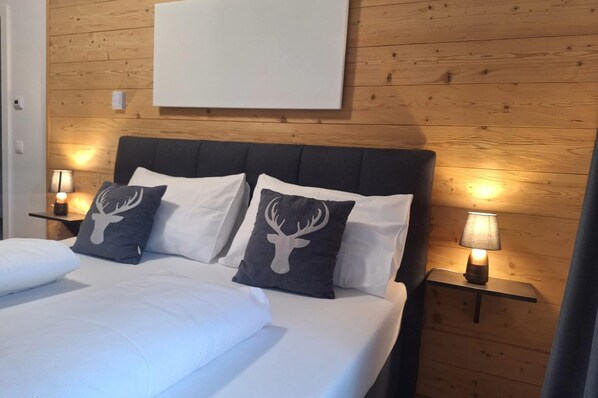 A bed with white bedding and two pillows, each with a deer head design, against a wooden wall. There are two bedside lamps on wooden nightstands. - Chalet in Turracher Hohe With Ski Slope Access (Reichenau)