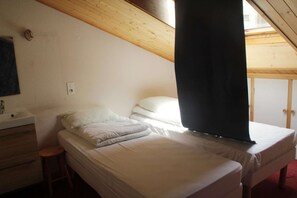 Ein Schlafzimmer mit zwei Betten, einer Holzbalkendecke, einer weißen Wand, einem kleinen Hocker und einem Fenster.