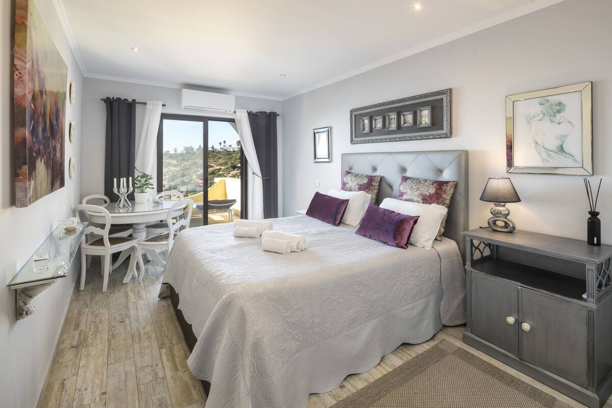 A bedroom with a bed, bedside table, lamp, and a view of the outdoors.
