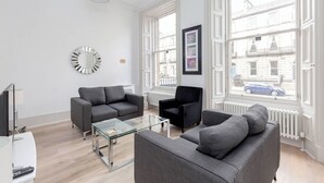 A modern living room with two grey sofas, a glass coffee table, a black armchair, and a large window with a view of buildings and a car. - 6 on Chester Apartments (Edinburgh)