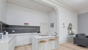 A modern kitchen with white cabinetry, a central island with stools, a grey sofa, and a decorative mirror. - 6 on Chester Apartments (Edinburgh)