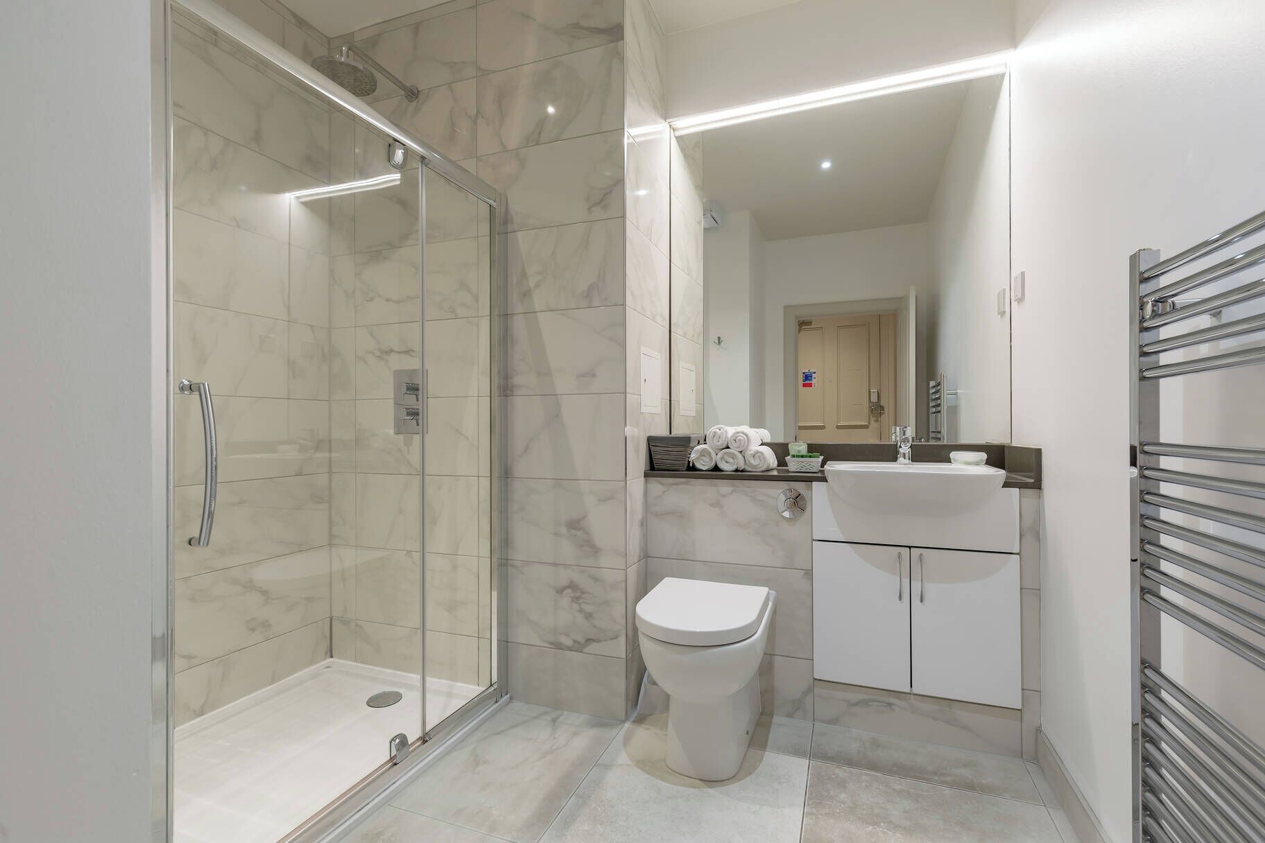 Une salle de bain moderne avec une douche à parois de verre, des toilettes, un lavabo et un porte-serviettes.