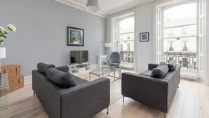 A modern living room with two grey sofas, a glass coffee table, a flat-screen TV, and a large window with a view of buildings. - 6 on Chester Apartments (Edinburgh)