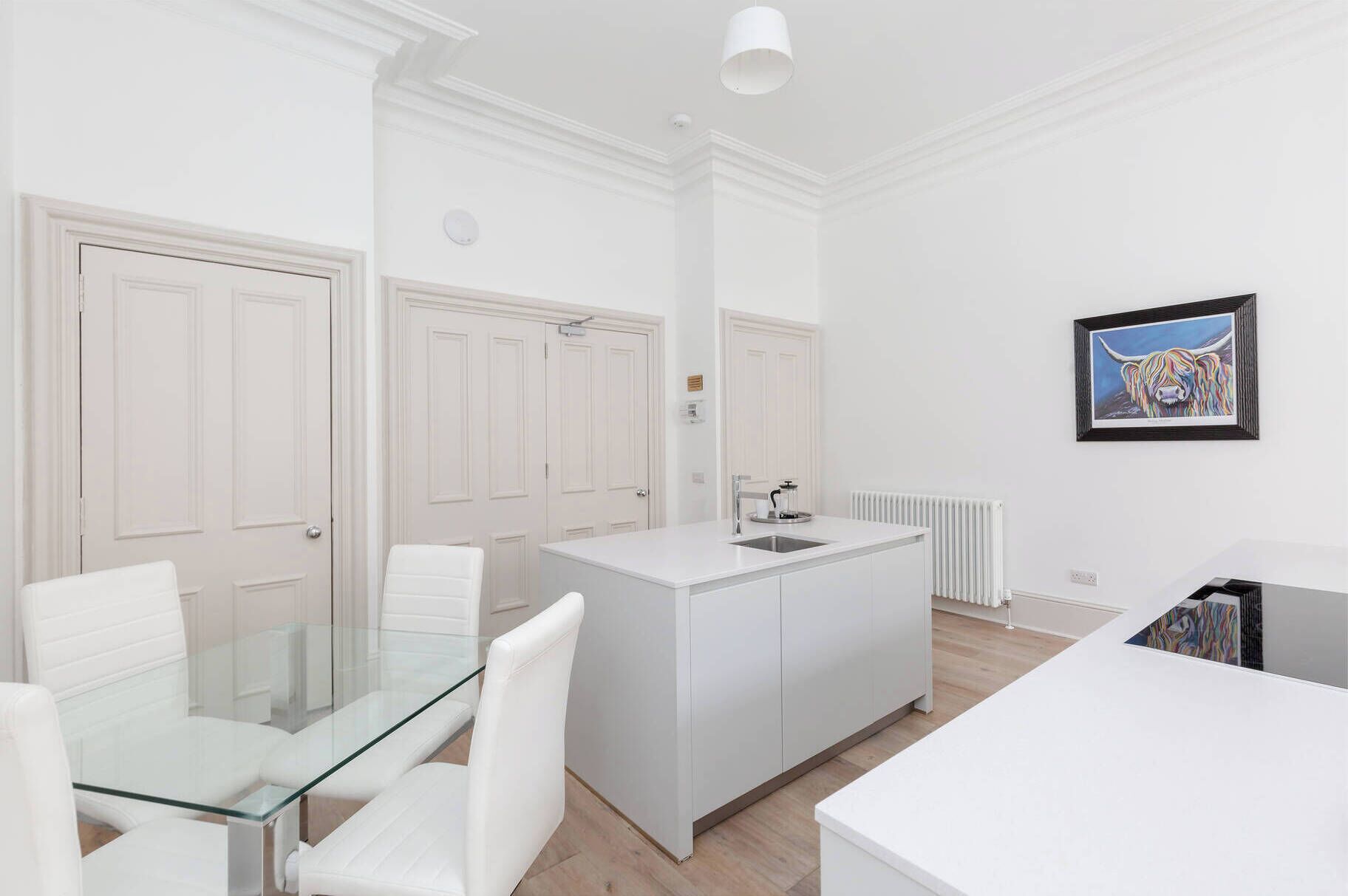 A modern kitchen with white cabinetry, a glass dining table, and a white island with a sink.