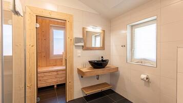 Une salle de bain avec une porte de sauna en bois, un lavabo noir, un miroir, une fenêtre et des toilettes.
