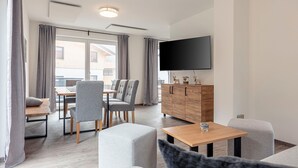 A modern living room with a flat-screen TV, grey upholstered furniture, a wooden cabinet, and a dining area with a table and chairs. - Chalet in St. Englmar With Private Sauna & Hottub (Sankt Englmar)