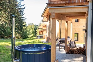 Una baita di legno con vasca idromassaggio, area salotto esterna e patio coperto.