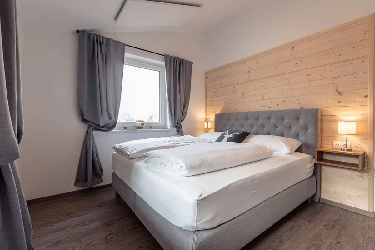 A bedroom with a large bed, grey curtains, a wooden headboard, and bedside lamps.