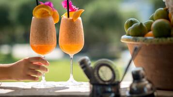 Two drinks with fruit garnishes and a fruit bowl on a table.