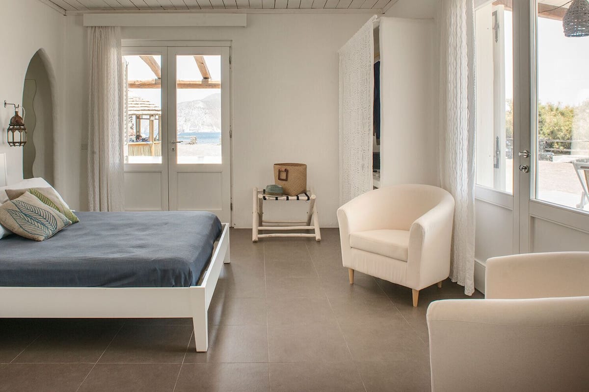 Un dormitorio con una cama, una silla, una mesita y vistas al exterior.