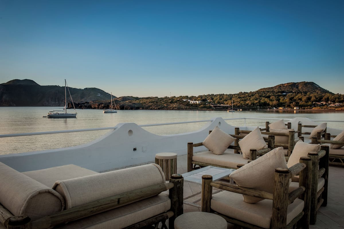 Una terraza frente al mar con sillas de madera y vistas al océano y colinas.