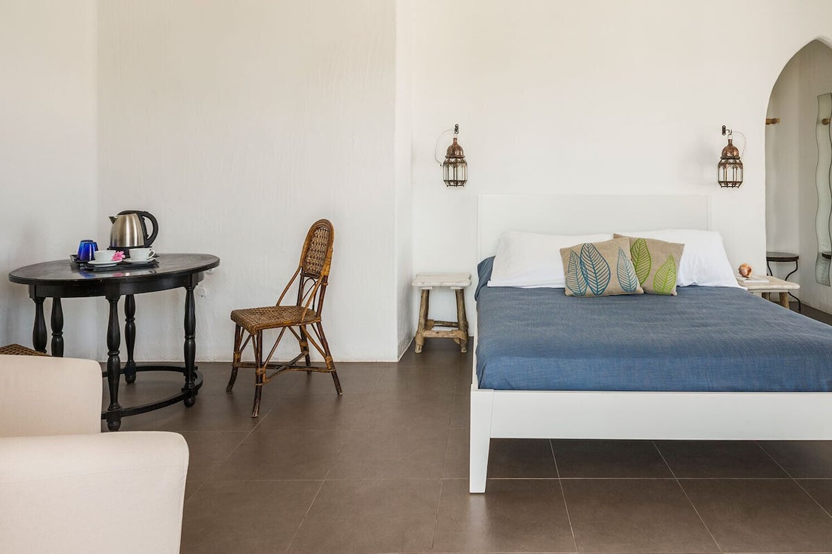 Un dormitorio con cama, una silla, una mesita con tetera y una mesita de noche.