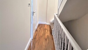 Ein Flur mit Holzboden, einer weißen Tür und einer Treppe mit weißen Spindeln.