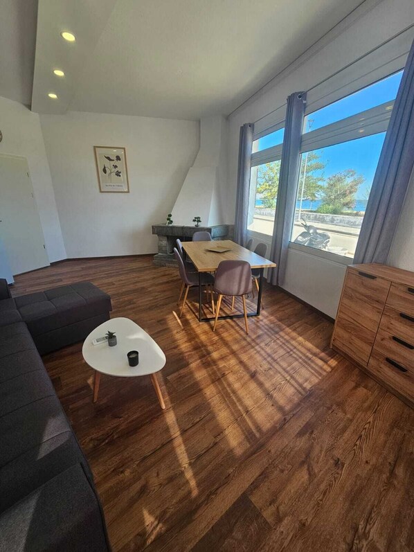 Un salon moderne avec un canapé, une petite table blanche, une table à manger avec des chaises et une vue dégagée grâce à de grandes fenêtres.