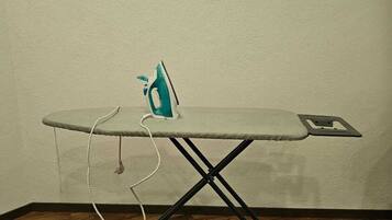 A small, foldable ironing board with an iron and a cord, placed on a wooden floor against a plain wall.