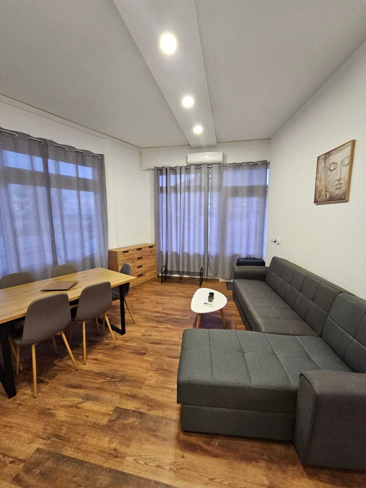 En moderne stue med et træspisebord, en grå sofa og et lille hvidt bord.