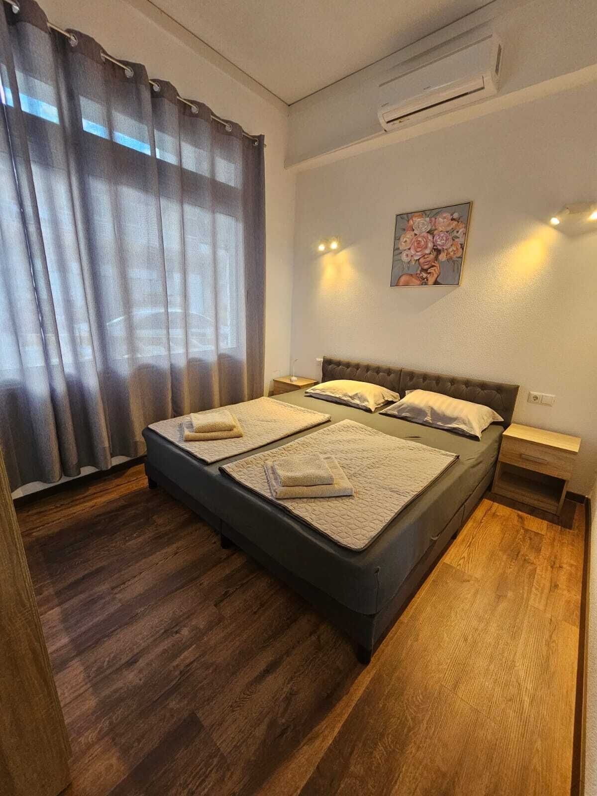 Un dormitorio con cama, suelo de madera, unidad de aire acondicionado, mesita de noche y un cuadro en la pared.