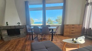 Ein modernes Wohnzimmer mit Kamin, Essbereich mit Stühlen, einer Couch und Meerblick.