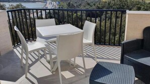 A balcony with a table and chairs, a view of a coastal landscape, and a railing.