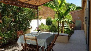 Un patio al aire libre con una mesa y sillas, rodeado de abundante vegetación y un techo de paja.