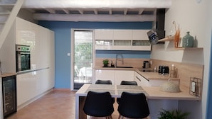 Una cocina moderna con armarios blancos, un rincón de comedor con dos sillas y un horno empotrado.