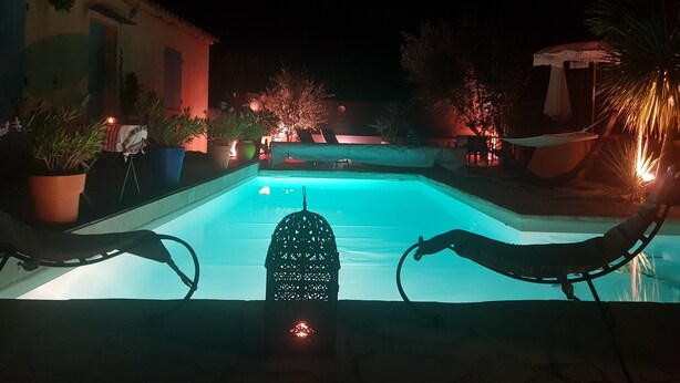 Una piscina con una fuente de agua, rodeada de plantas en macetas y mobiliario de exterior.