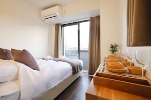 Una habitación de hotel con cama, ventana, aire acondicionado y una bandeja con cuencos y copas de vino.