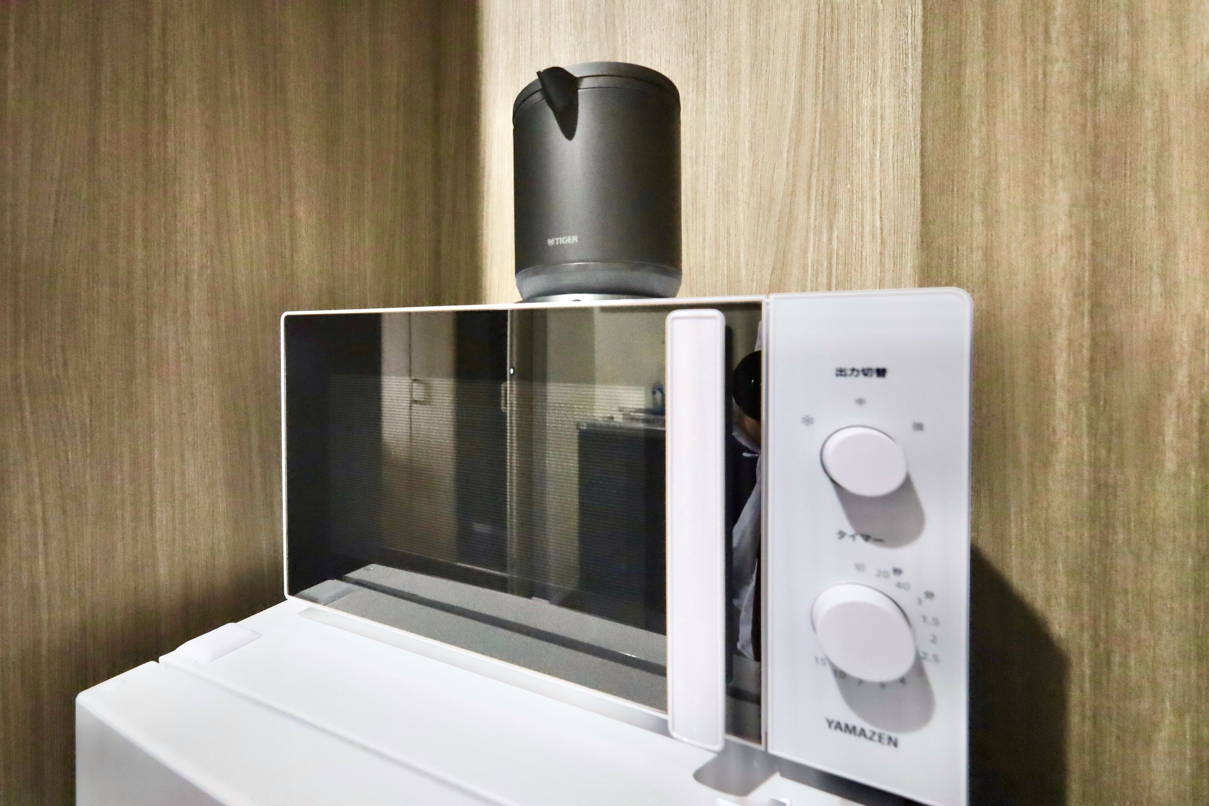 A microwave with a digital display and control panel, placed on a white surface against a wooden wall.