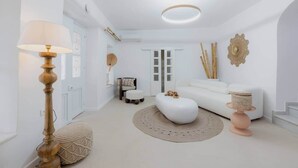 En moderne stue med en hvid sofa, et rundt sofabord, en gulvlampe og en dekorativ vægdekoration.