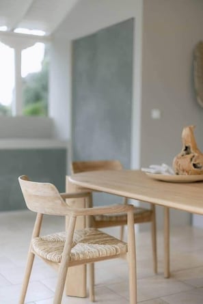 Un coin repas avec une table et des chaises en bois, un vase posé sur la table et une vue sur la verdure à l’extérieur.