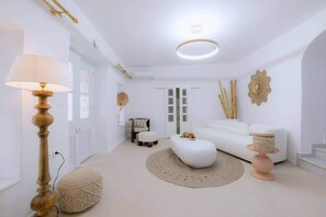 Ein modernes, weißes Wohnzimmer mit rundem Couchtisch, einem weißen Sofa, einer Lampe und einem Wandkunstwerk.