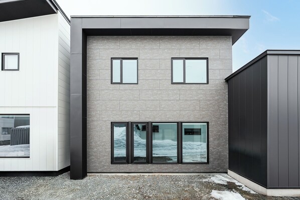 Un bâtiment moderne aux façades extérieures combinant des couleurs blanche et grise, de grandes fenêtres et un sol recouvert de gravier.