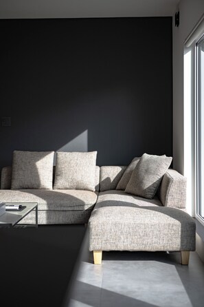 A modern living room with a sectional sofa, a coffee table, and a large window providing natural light. - U suzukou (Asahikawa)