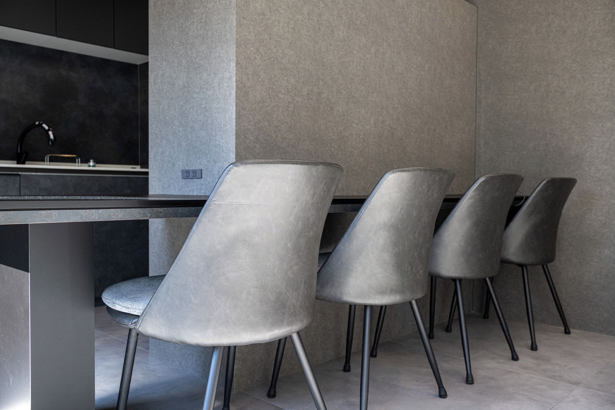 A modern kitchen with a dark countertop and four grey chairs with metal legs.