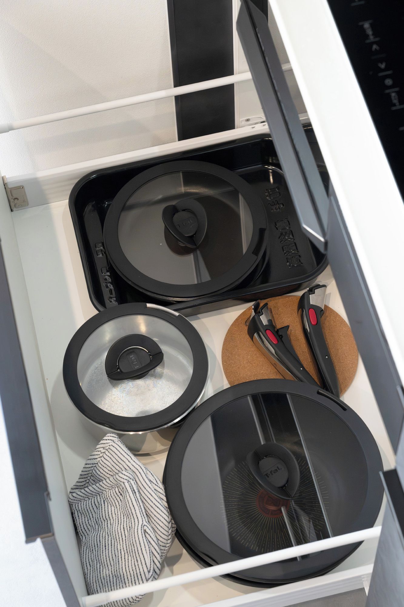 A kitchen drawer with three black lids, a striped cloth, and a cork mat.