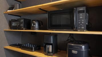 A kitchenette with wooden shelves, a microwave, a coffee maker, and a toaster.