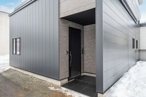 Un bâtiment moderne à l’extérieur gris, avec une porte noire et une petite fenêtre.