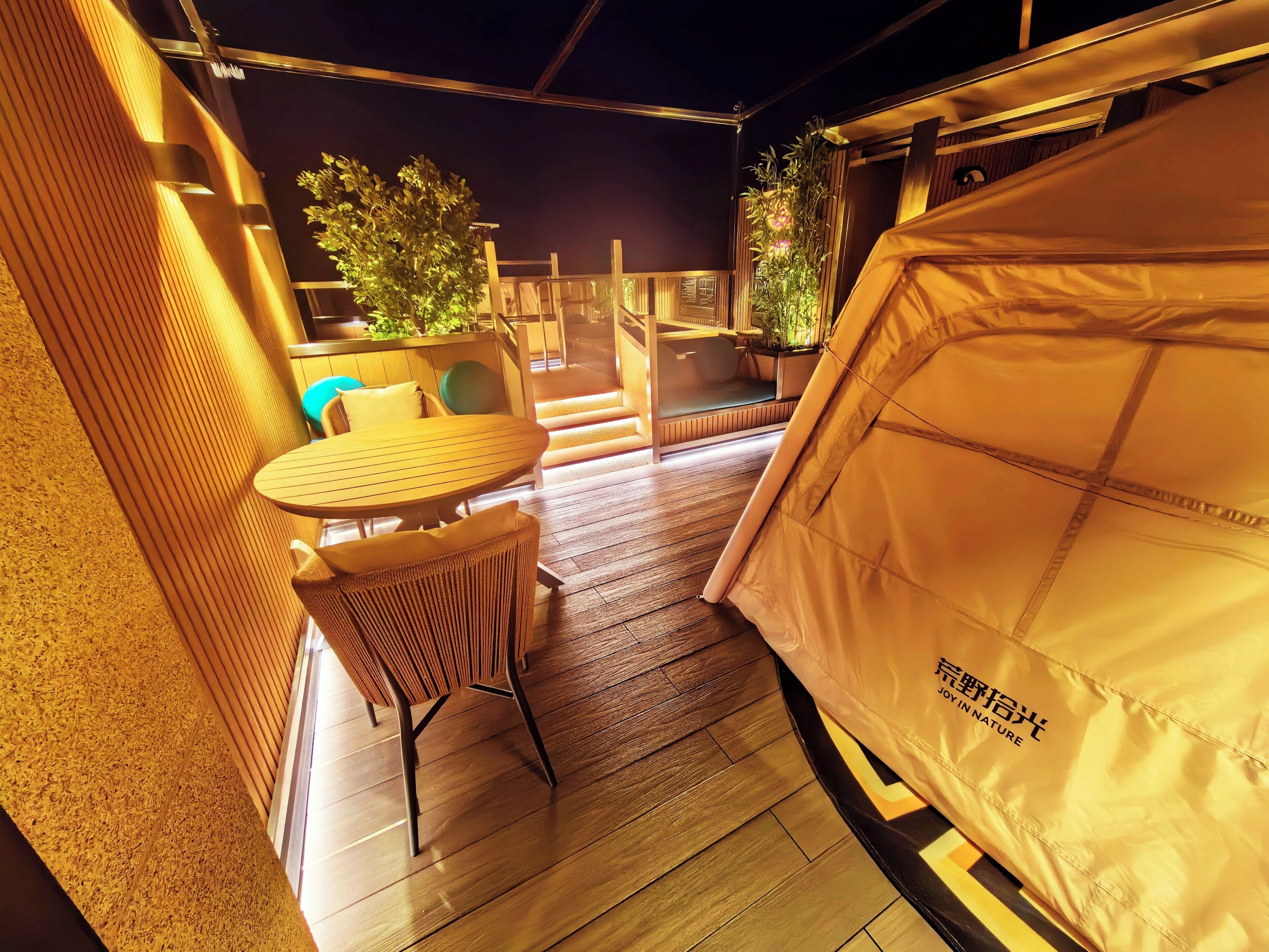 A tented outdoor area with a table and chairs, wooden flooring, and potted plants.