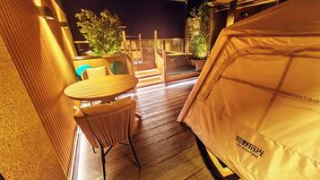 A tented outdoor area with a table and chairs, wooden flooring, and potted plants.
