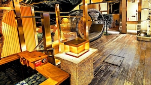A wooden bench, a stone pedestal, and a woven chair in a room with a wooden floor and a glass door leading outside. - Tsuruyoshikawa onsen hotel (Manazuru)