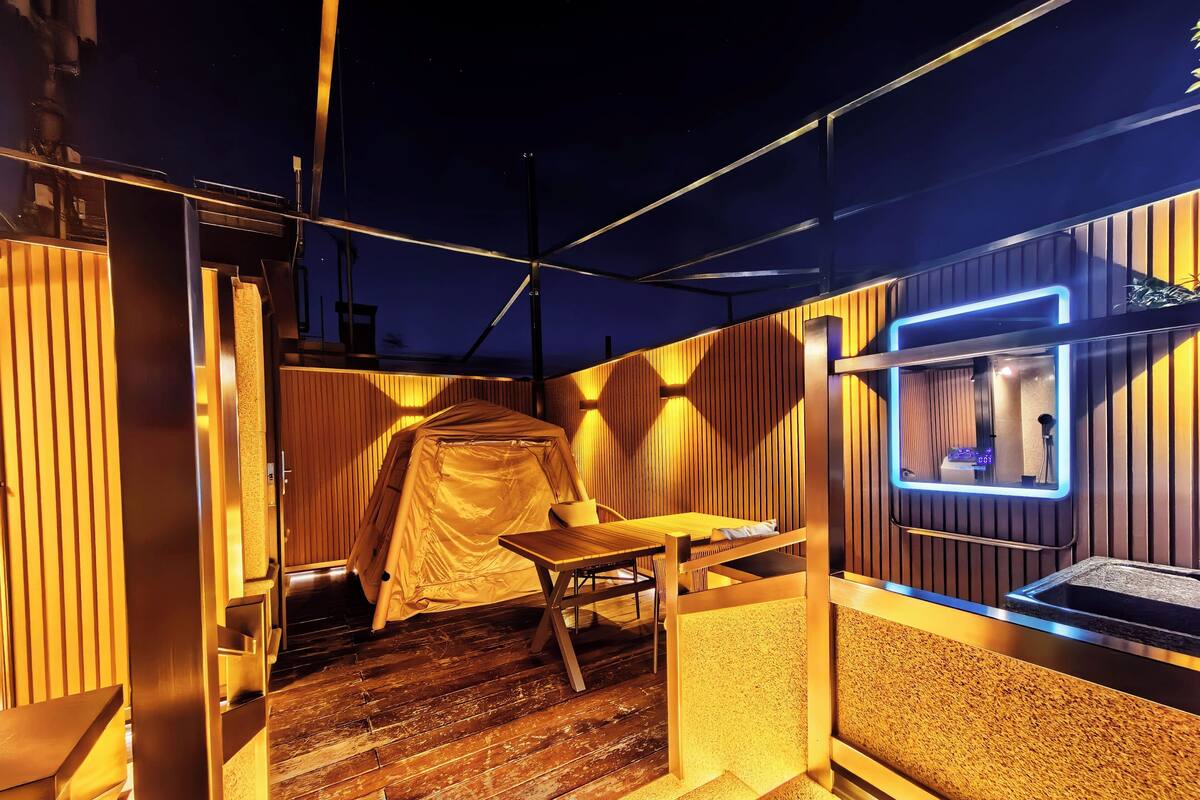 Een tentachtige buitenruimte met een tafel en stoelen, houten lambrisering en een raam met neonverlichting.