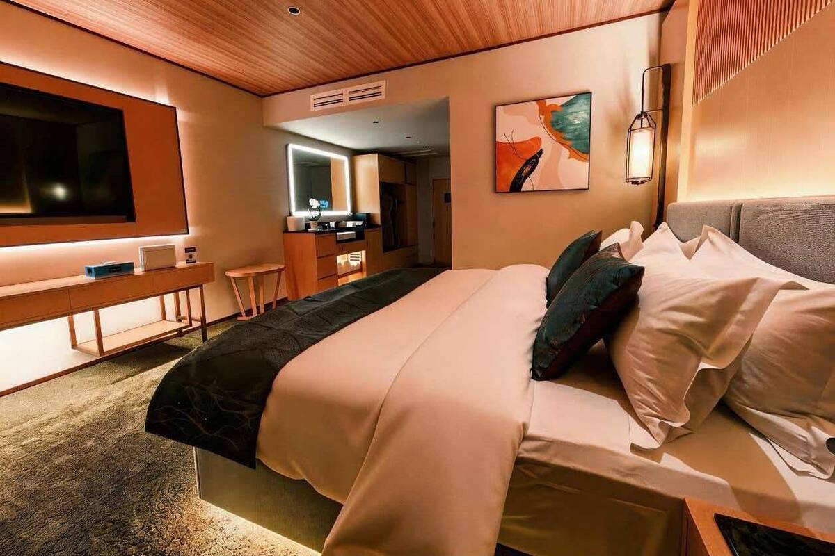 Een moderne hotelkamer met een bed, nachtkastje, televisie, bureau en stoel.