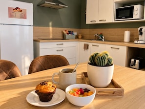 A kitchen with a microwave, a refrigerator, a coffee maker, a cactus, a muffin, and a bowl of fruit. - San Francisco - Apartment in a complex with a pool (Neuf-Mesnil)